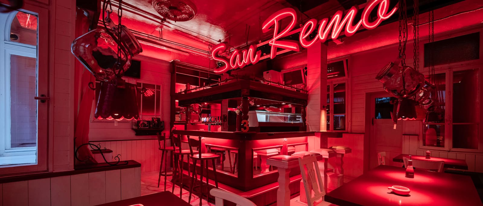 Gastraum mit Bar, Tischen und Neonschriftzug in rotem Licht